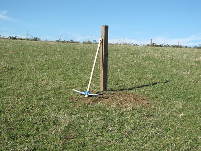 Poteau carré dans un grand pré avec une pioche.